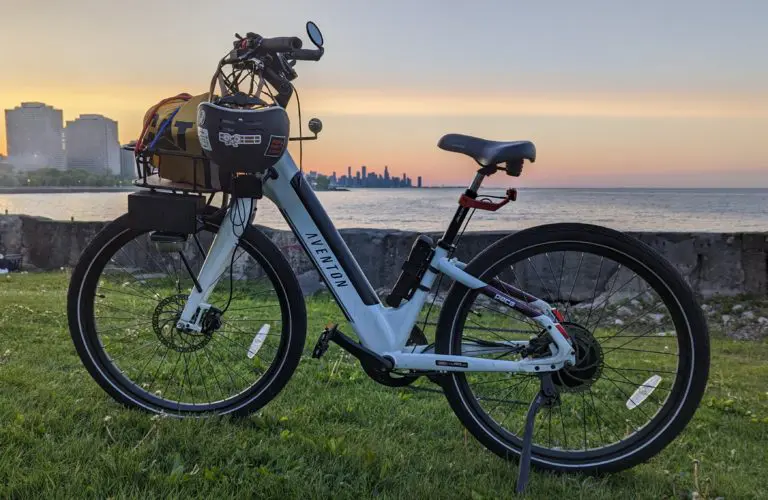 A white bike with a helmet sitting on grass by the Chicago lakefront at sunset.