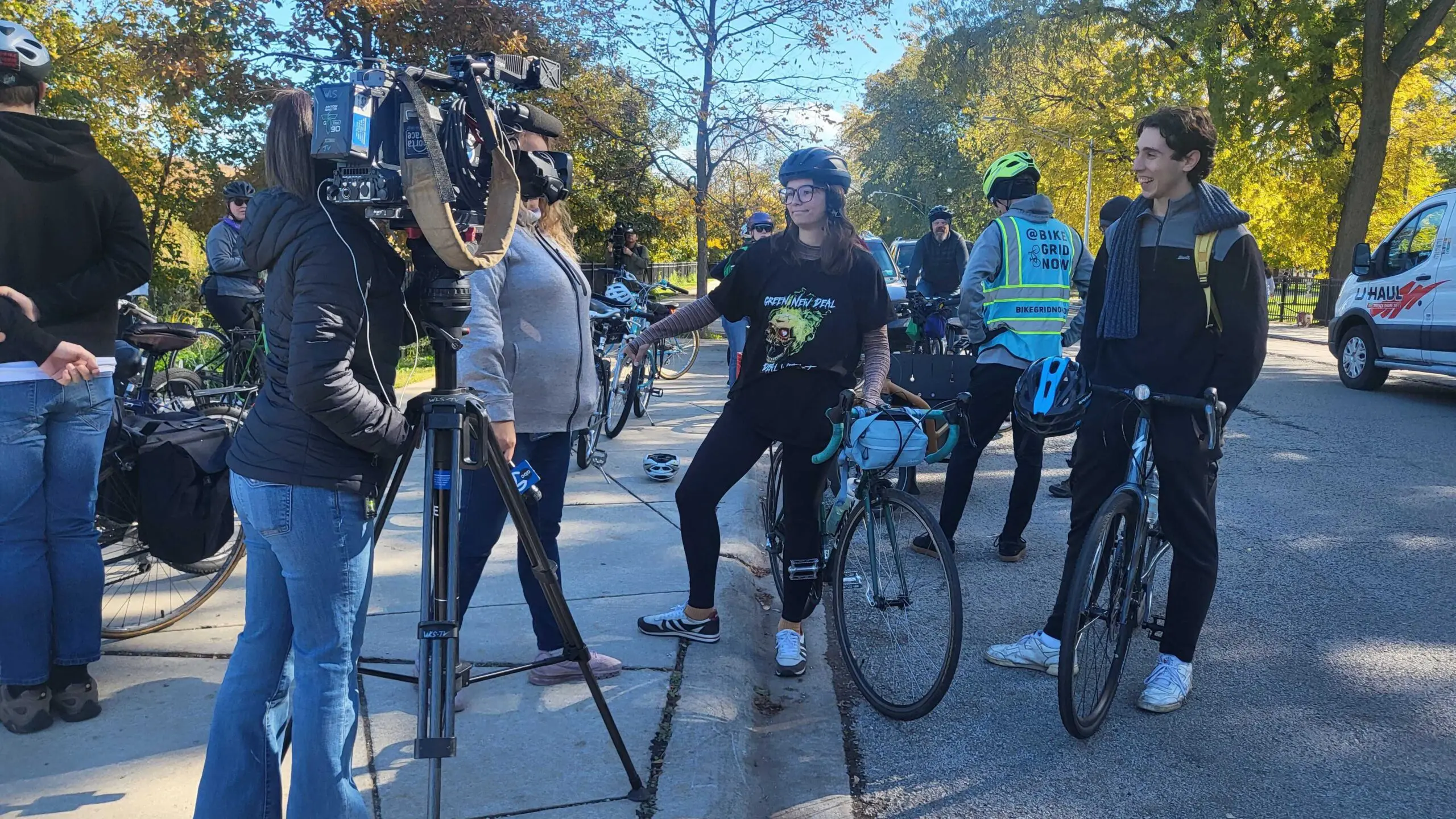 Two bikers are interviewed in front of a television camera before a group ride.